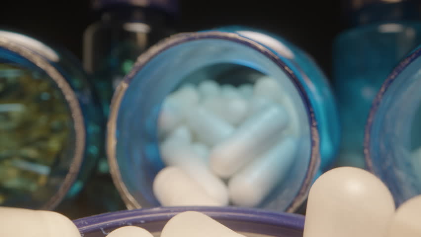 Fingers Picking a White Capsule from a Blue Lid Filled with Capsules and Surrounded by Supplement Bottles, Closeup Macro View Dolly slider, close up.