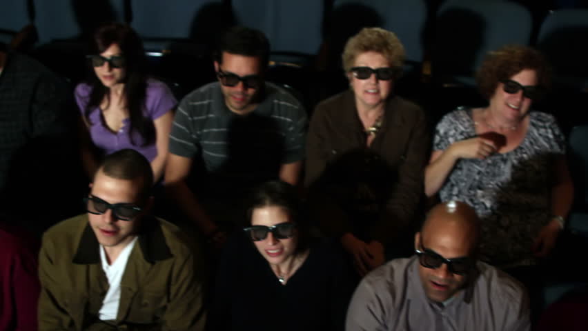 Happy audience watching a 3D movie in a theater. Camera moves on a jib and