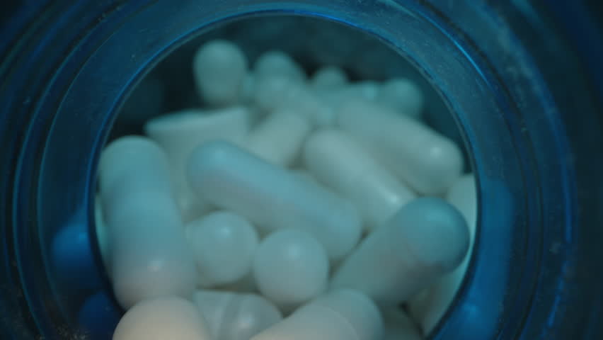 White Capsules Pouring from a Blue Bottle into a Lid, Captured in Sharp Macro Focus with Smooth Illumination Against a Dark Background. Wellness and Healthcare