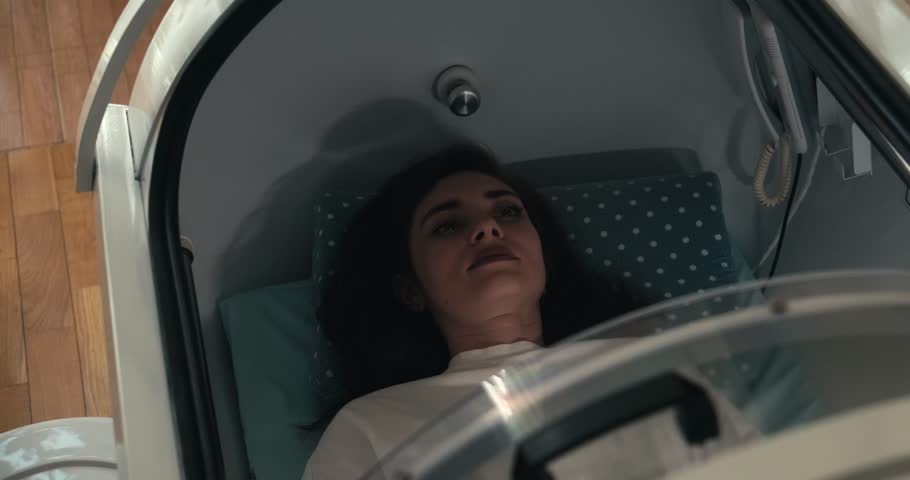 A young woman lying inside a hyperbaric oxygen chamber, seen through the glass. Represents medical treatment, wellness therapy, and advanced healthcare technology