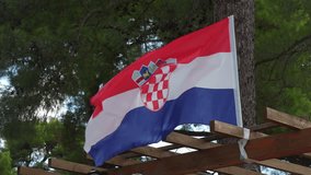 Croatian flag waving in the wind with backdrop of pine tree crowns in slow motion. Concept of patriotism, natural beauty, and national pride. High quality 4k footage - Powered by Shutterstock - Get 15% off with code: PIKWIZARD15