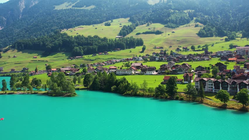 Drone footage of turquoise clear lake Lungern or Lungerersee in Switzerland in summer sunny day with village and green meadow