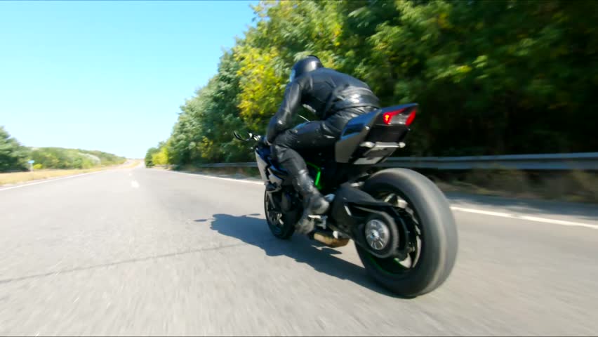 Aerial shot of man riding fast on modern sport motorbike at highway during summer day. Motorcyclist racing his motorcycle on country road. Guy drive bike during trip. Concept of freedom and adventure