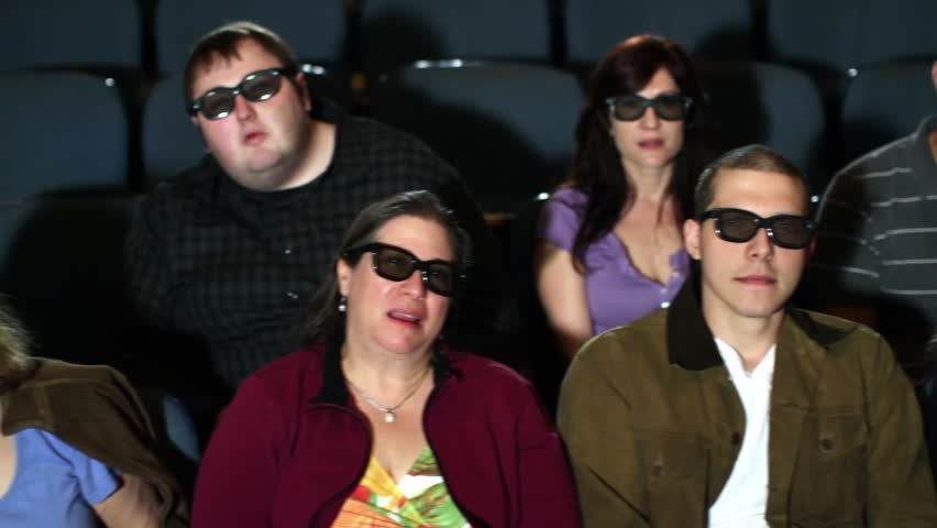 Curious audience watching a 3D movie in a theater. Camera moves on a jib and