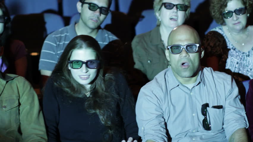 Audience reaction with emphasis on young woman at 3D movie screening. Camera