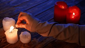 Close up shot of wooden table in darkness with red and white candles, woman hand holding lighted match and lightning candles. - Powered by Shutterstock - Get 15% off with code: PIKWIZARD15