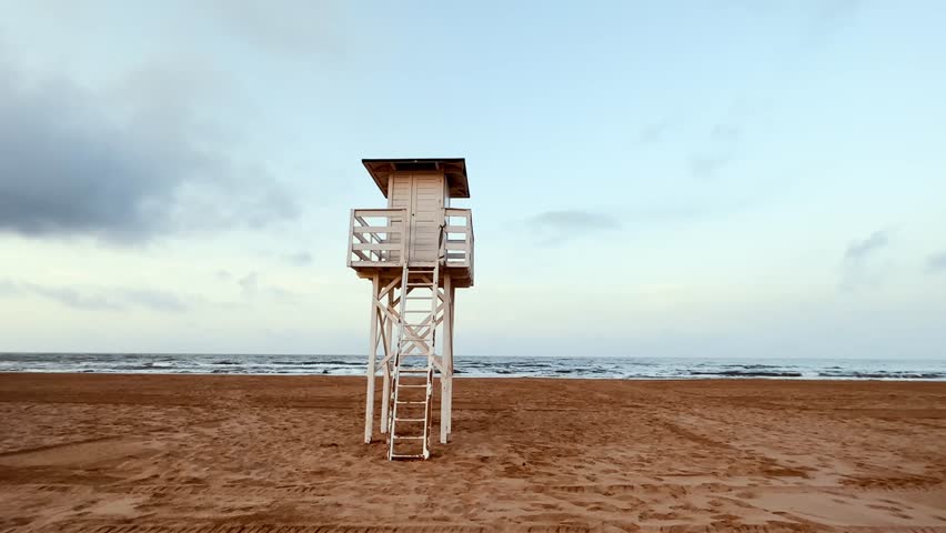 A white wooden lifeguard watchtower located on the beach. A rescue station on the ocean coast in the morning. Empty coastline. Summer holidays on sea 