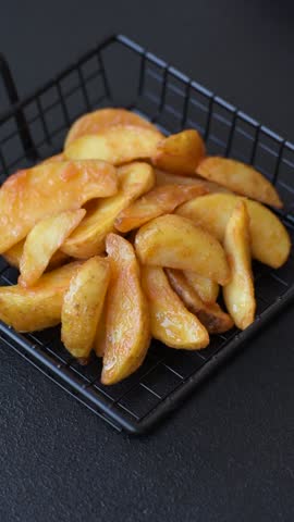 Baked potato wedges with cheese and herbs on a dark background. Homemade organic vegetable vegan vegetarian potato wedges