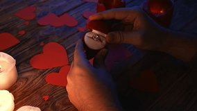 Close up of wooden table in darkness with red and white lighted candles and scattered red paper hearts, man holding and opens jewelry box with diamond ring inside. - Powered by Shutterstock - Get 15% off with code: PIKWIZARD15