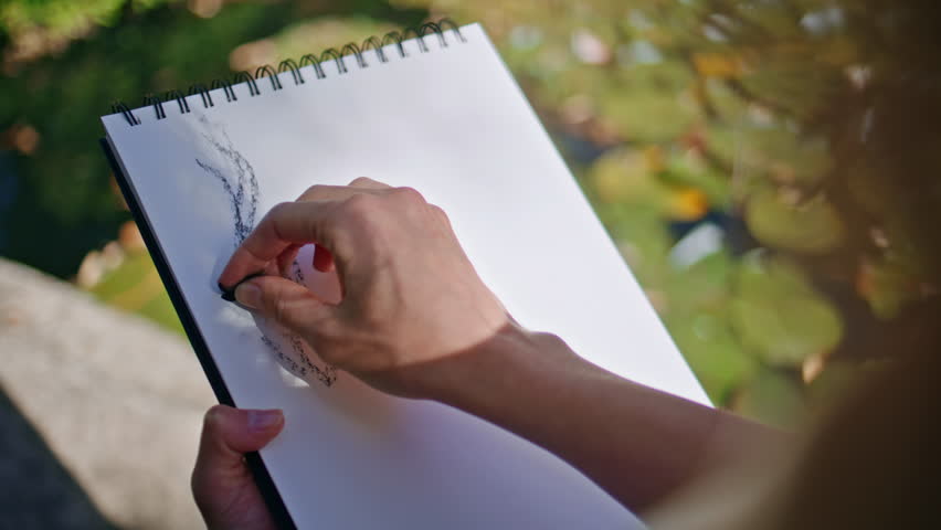 Artist hands drawing sketch on paper at sunshine nature closeup. Young woman fingers painting picture with pencils in summer place. Unrecognizable girl enjoying creative hobby alone. Art concept 