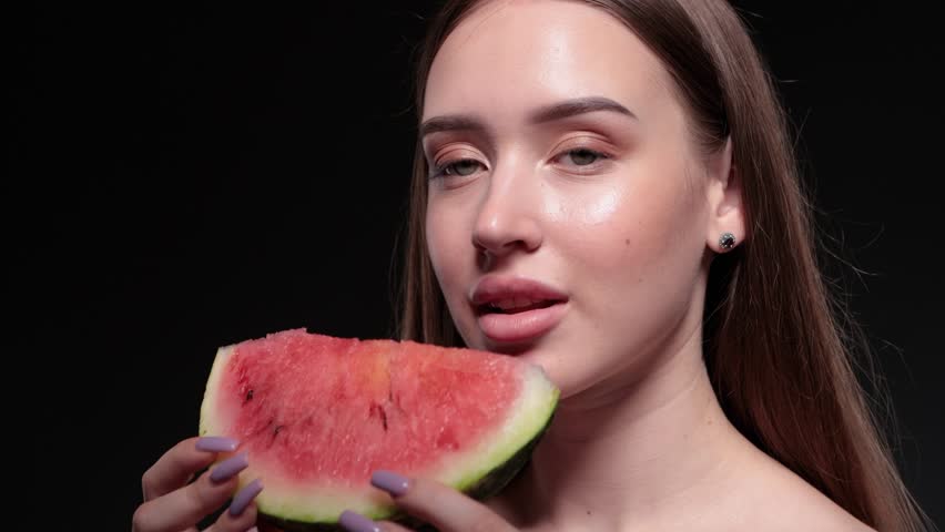 Beautiful young girl eats a ripe juicy watermelon on a dark background.