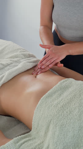 Therapist performing lymphatic drainage massage on patient's belly. This has a number of benefits such as reducing inflammation and fluid retention. Close up. Vertical video.