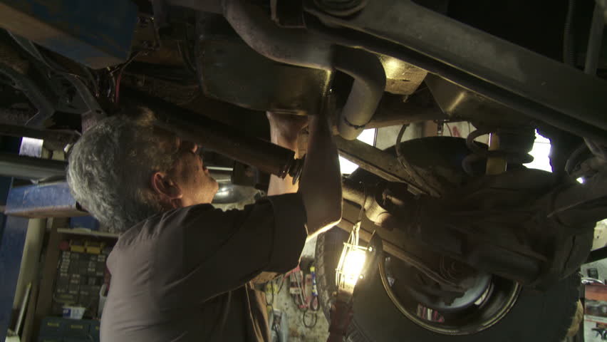 Auto mechanic working on the underside of a car. Hand held shot.