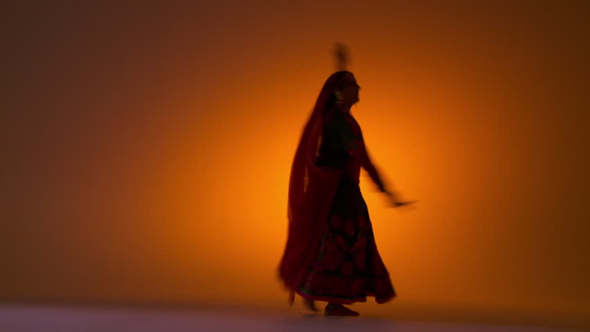 Indian girl in traditional folk costume spins as she dances against an orange