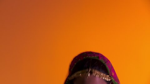Indian girl in traditional folk costume dances energetically an orange colored background with flashing lighting. Full length shot.