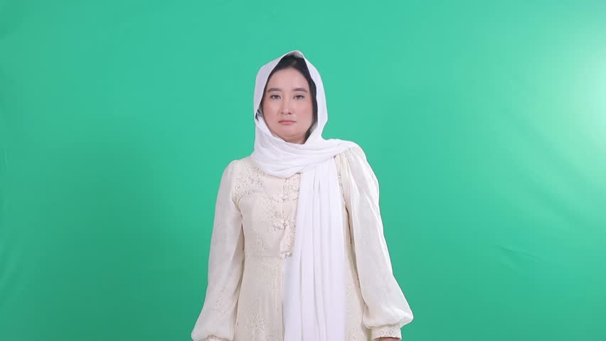 Indonesia muslim woman wearing hijab angry expression, glaring eyes, clenched fists looking at camera isolated on green background, green screen