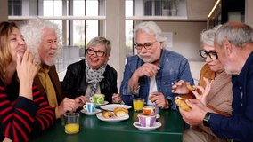 Group of joyful elderly friends gathered on terrace of residence cafeteria eating and drinking coffees and pastries. Caucasian seniors people meeting enjoying snack sitting together at table - Powered by Shutterstock - Get 15% off with code: PIKWIZARD15