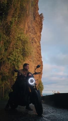 Vertical video of active young man standing on a motorcycle with Angels waterfall in Madeira in the background at sunset. Perfect for lifestyle, travel  and adventure in Madeira island 