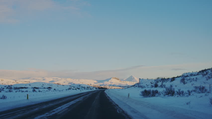 Snowy Icelandic road under Arctic sunset skies, peaceful winter journey through frozen landscapes, driving POV