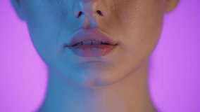 Slow motion 4K macro shot of a woman's smiling lips, vibrant purple background with soft blue and pink lighting on her face, cinematic and artistic close-up, glowing hues, and vivid color details - Powered by Shutterstock - Get 15% off with code: PIKWIZARD15