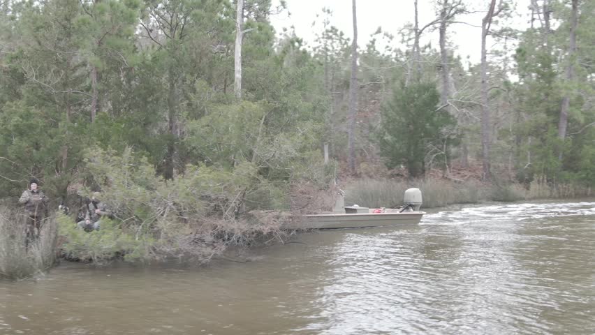 A hunter unloads gear from his camouflaged boat in a misty swamp, surrounded by mossy trees and calm waters, preparing for an adventurous day in the heart of the wilderness.
