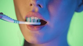 Slow motion 4K macro shot of a woman brushing her teeth with a toothbrush, vibrant green background with glowing pink and blue neon light on her face, cinematic and clean, detailed close-up aesthetic - Powered by Shutterstock - Get 15% off with code: PIKWIZARD15