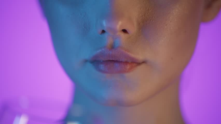 Slow motion 4K macro shot of a woman drinking pure water from a transparent glass, vibrant purple background with soft blue and pink lighting on her face, cinematic and refreshing aesthetic, close-up