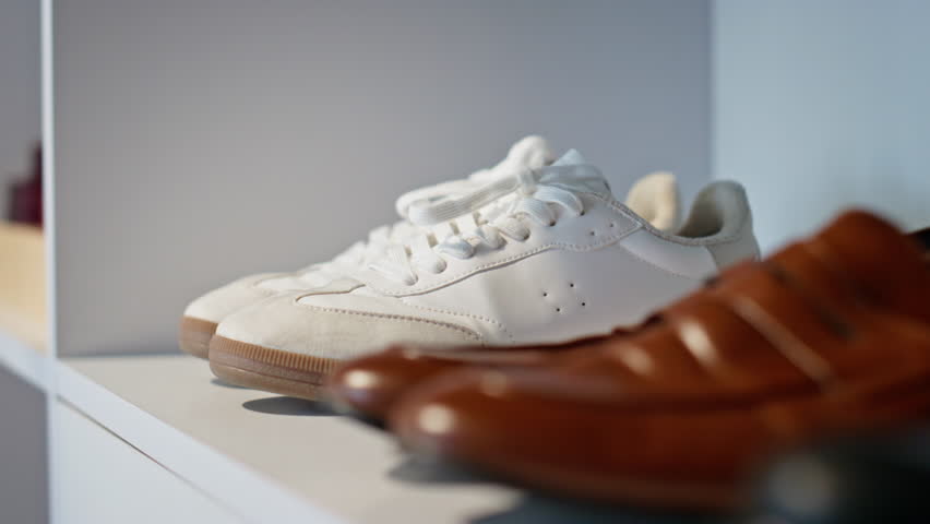 Leather shoes standing shelf in rich person wardrobe closeup. Different colours male footwear placed white modern closet. Three pairs of elegant luxury boots in store. Business people fashion concept