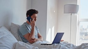 Upset manager speaking mobile phone sitting bed with laptop at hotel room closeup. Worried sad man having bad cellphone conversation discussing business problems. Sick employee working from bedroom - Powered by Shutterstock - Get 15% off with code: PIKWIZARD15