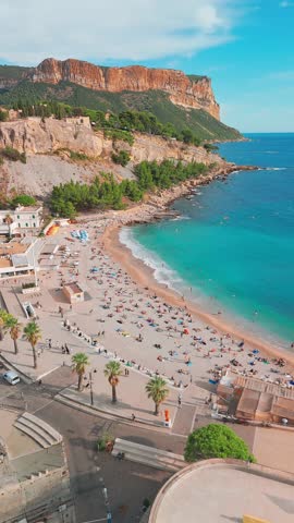 Aerial view of Cassis on the French Riviera, southern France. The scene features a medieval castle perched on a cliff, a sandy beach, turquoise sea waters, and the historic buildings of the town