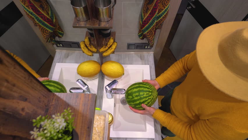 Wash a ripe watermelon under the water tap, top view. Male hands wash melon and watermelon fruit. Slow motion.