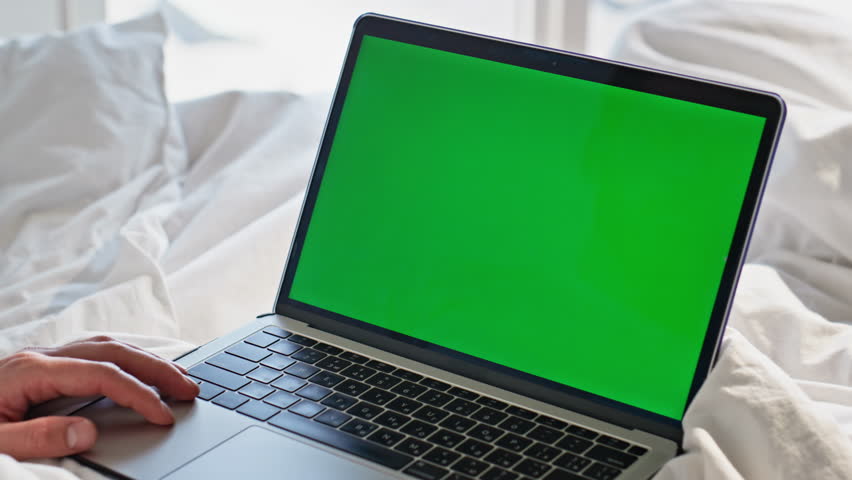 Closeup greenscreen laptop lying bed. Unknown man watching chroma key computer resting at comfortable blanket. Male person enjoying webinar alone at white beddings morning. Online work in cozy bedroom