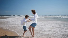 Mother spinning happy boy stepping on foamy ocean waves. Playful family bonding having fun together at beautiful sandy beach. Smiling mom enjoying energetic activity with beloved son at summer shore. - Powered by Shutterstock - Get 15% off with code: PIKWIZARD15