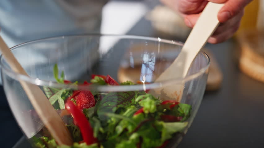 Chief hands mixing salad preparing food at cozy kitchen closeup. Carefree cheerful guy preparing vegetables cooking at light apartment. Smiling brunette making tasty meal alone. Culinary concept 