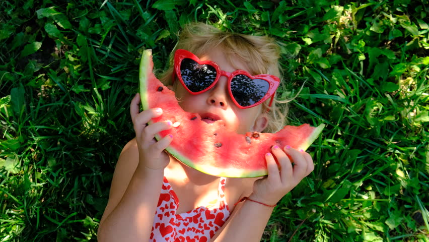 Child in sunglasses eating watermelon in the garden. Selective focus.