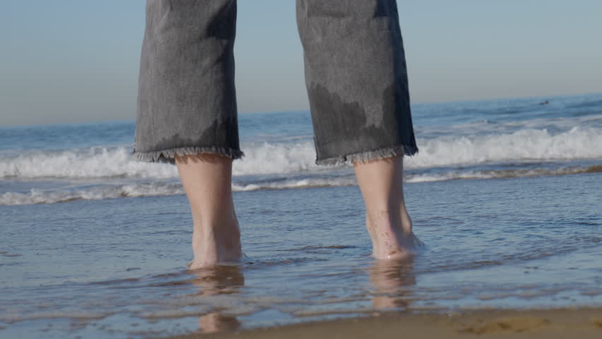 Woman walking towards the sea, her dog circling around her. On a winter
