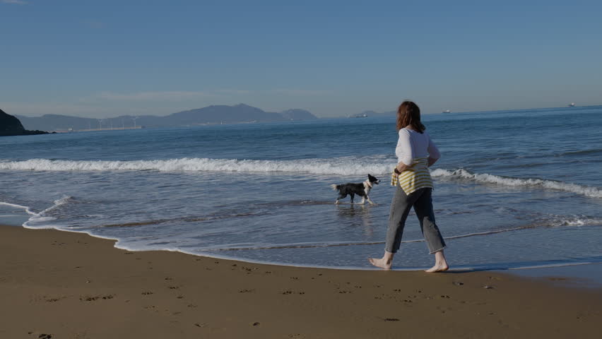 Woman happily walking her dog along the beach on a sunny spring day. Looking out to sea.