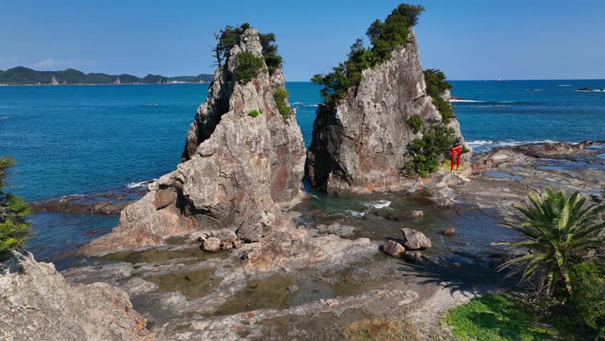Cliffs in the ocean off the coast of Japan with traditional red tori gate, aerial view of Japanese coastline