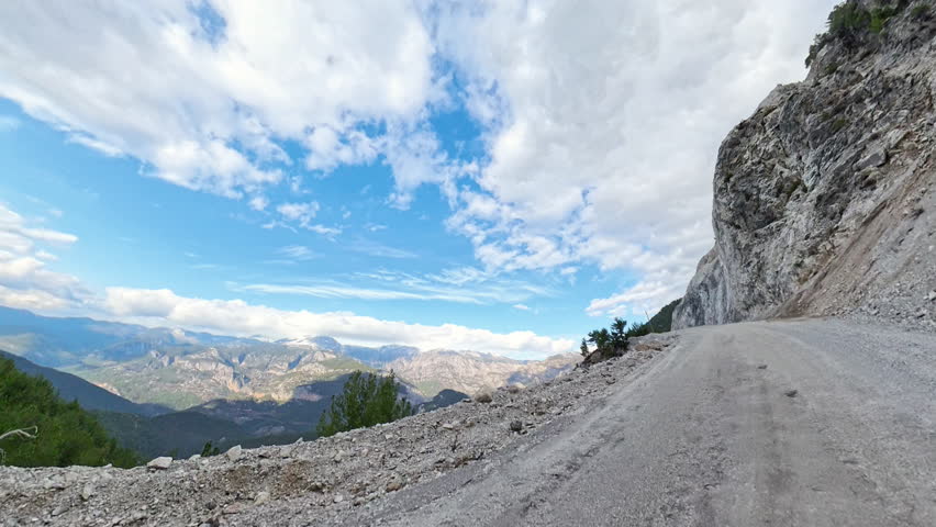 Dirt road on the edge of a steep cliff with panoramic views of a vast valley and distant mountain ranges, under a clear blue sky with scattered clouds. Cliffside Drive