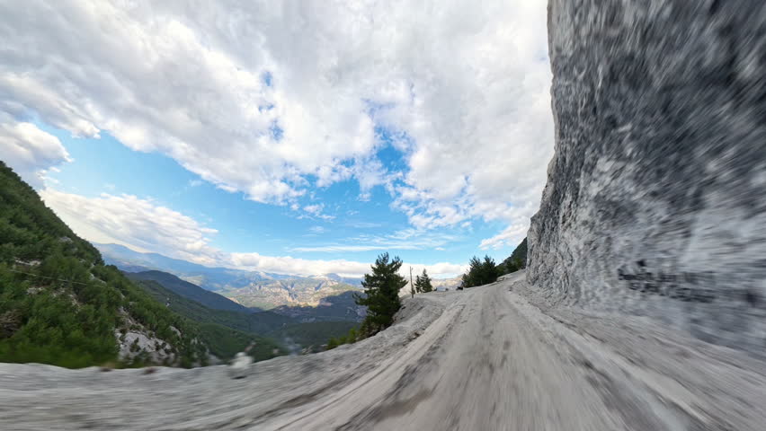 Dirt road on the edge of a steep cliff with panoramic views of a vast valley and distant mountain ranges, under a clear blue sky with scattered clouds. Cliffside Drive