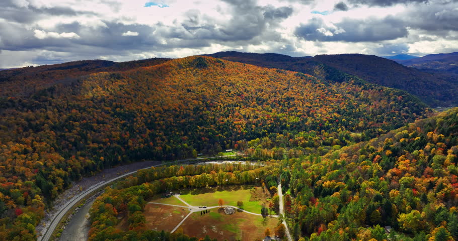 Colorful trees cover the mountain slopes. Dramatic clouds float in the sky above the rocks. Autumn in nature. Aerial view.