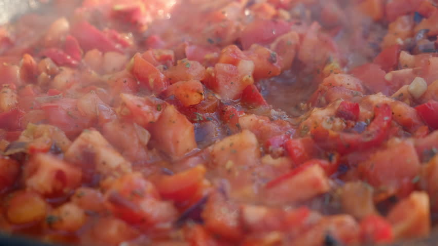 Cut tomatoes with red peppers and spices languishing in pan on bonfire at nature. Camping vibes, nature and outdoor lifestyle mood. Cooking outdoors concept