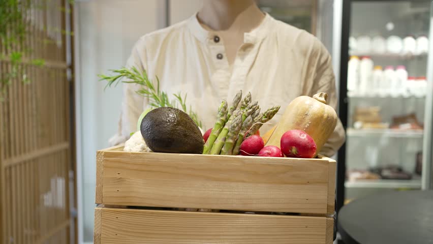Professional chef presenting wooden crate filled with vibrant, farm-fresh organic vegetables in restaurant kitchen, showcasing colorful local produce