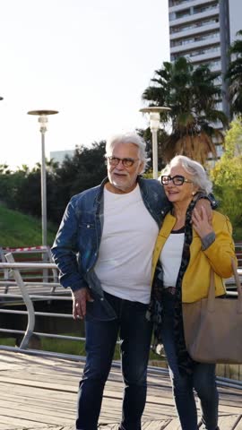 Vertical. Happy adult Caucasian elder couple stroll embraced walking for park the in city. Retired mature people in love enjoying romantic getaway. Positive relationships and spring retiree holidays