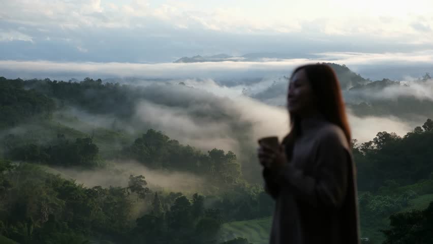 Blurred of a woman drinking coffee and looking at a beautiful mountain views on foggy day