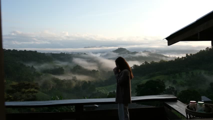 A woman drinking coffee and looking at a beautiful mountain views on foggy day