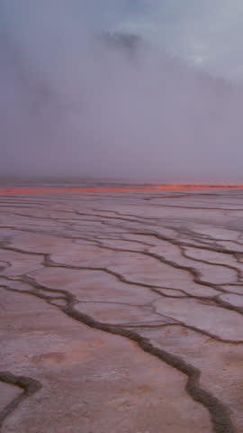 A serene, breathtaking landscape within Yellowstone National Park showcases cracked earth alongside rising steam, which together create an otherworldly atmosphere in Wyomings stunning natural beauty
