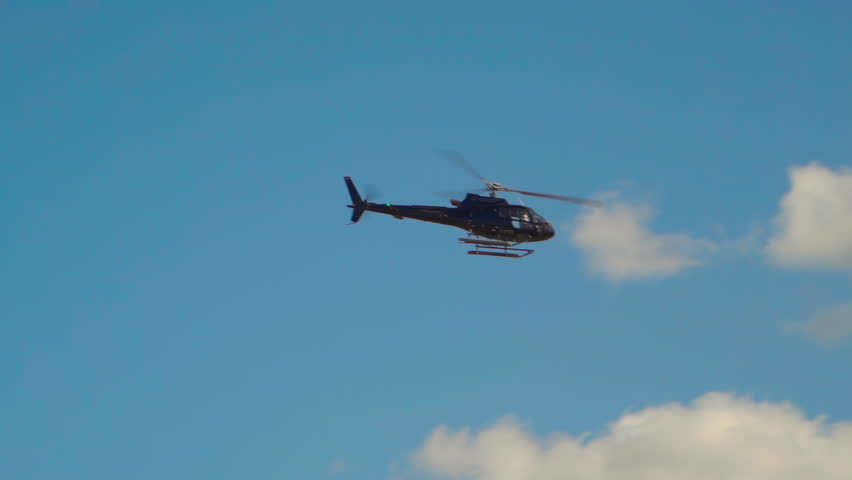 Helicopter flying in a clear blue sky above fluffy clouds during afternoon hours