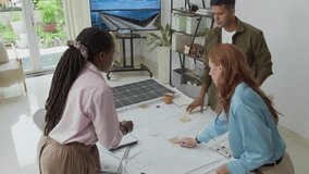 Static shot of three multiracial engineers in casualwear discussing blueprints of solar panels while standing by desk at alternative energy office - Powered by Shutterstock - Get 15% off with code: PIKWIZARD15