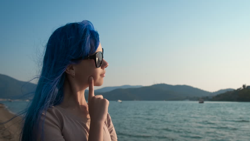 The girl on the seashore thinks. A young teenage girl with blue hair looks thoughtfully into the sea.